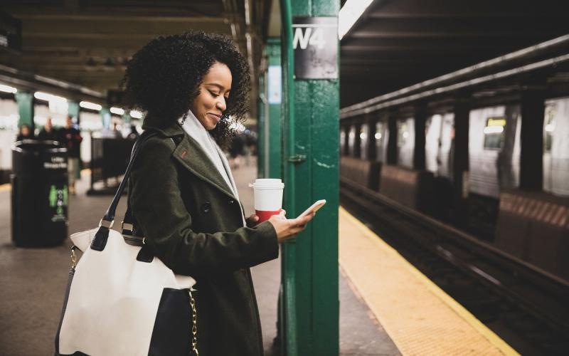 woman with a cup of coffee texts on subway station platform