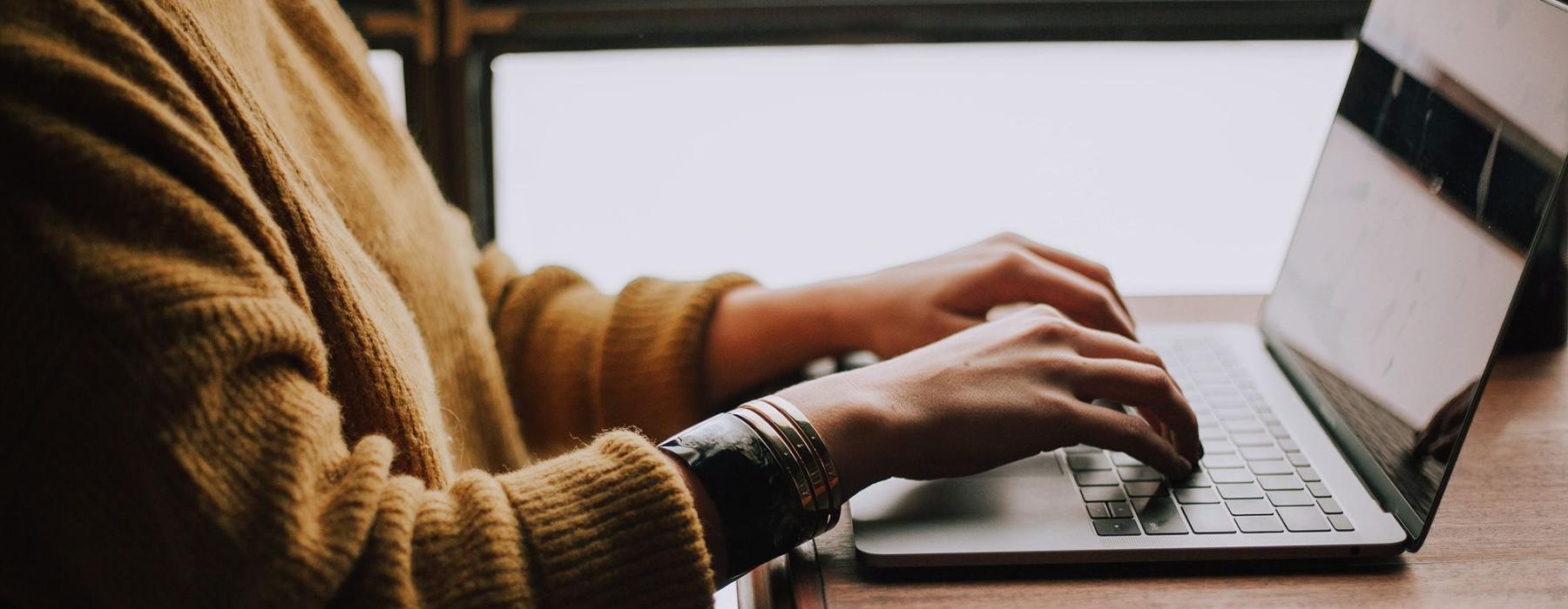 woman types on her laptop near large window